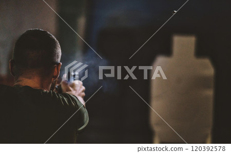 Man shooting a firearm at a shooting range. The person is aiming at a target silhouette. visible smoke near the firearm, likely from a recent shot. 120392578