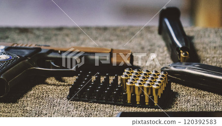 handgun, ammunition, and a magazine. The ammunition is arranged neatly in a tray holder. The handgun and the magazine appear to be placed on a surface, possibly a table or countertop. 120392583