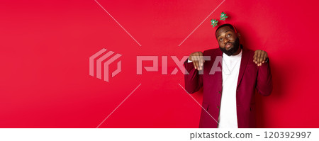 Merry Christmas. Silly and funny Black man in party headband, imitating bunny or cute puppy, standing over red background 120392997