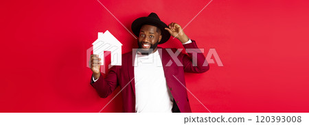 Real estate. Cheerful Black man showing paper house and smiling, recommending broker, standing over red background Real estate. Cheerful Black man showing paper house and smiling, recommending broker, standing over red background 120393008