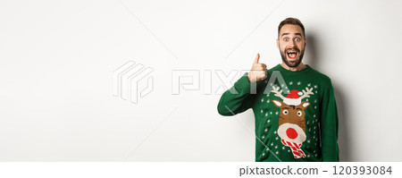Winter holidays and christmas. Excited caucasian guy showing thumb up and looking amazed, standing in green sweater against white background 120393084