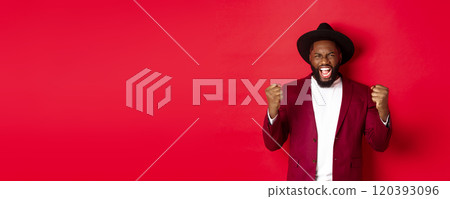 Satisfied lucky Black man celebrating victory, screaming from rejoice, winning prize, saying yes and fist pump, red background Satisfied lucky Black man celebrating victory, screaming from rejoice, winning prize, saying yes and fist pump, red background 120393096