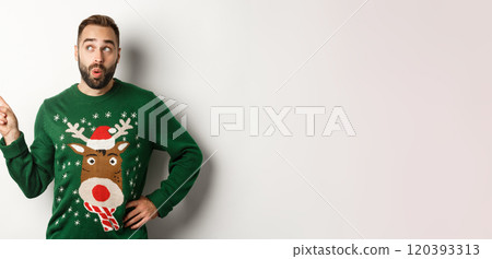 Winter holidays and christmas. Man looking curious at New Year shopping promo, standing in funny sweater against white background 120393313