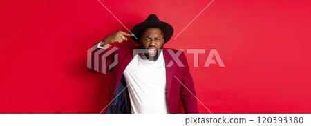 Angry Black man scolding person for being stupid, pointing at head and looking pissed-off, standing against red background Angry Black man scolding person for being stupid, pointing at head and looking pissed-off, standing against red background 120393380