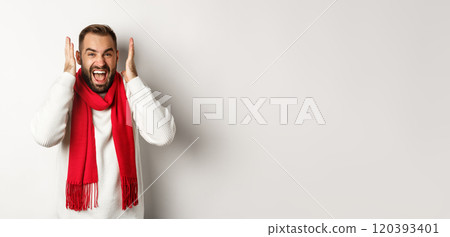 Christmas holidays and New Year concept. Angry man in scream and shout, shaking hands near head with frustrated expression, standing over white background 120393401
