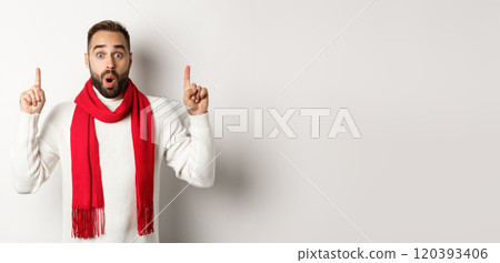 Christmas shopping and winter holidays concept. Surprised male model with beard pointing fingers up, saying wow, looking impressed at camera, white background 120393406