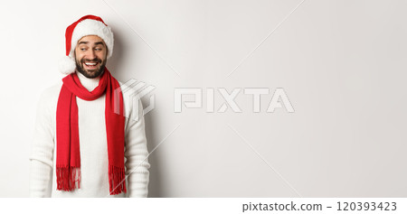 Winter holidays and New Year party concept. Man looking intrigued to the left, wearing Santa hat and celebrating Christmas, standing over white background 120393423