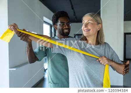 Female patient working with stretching band, male doctor helping her 120394384