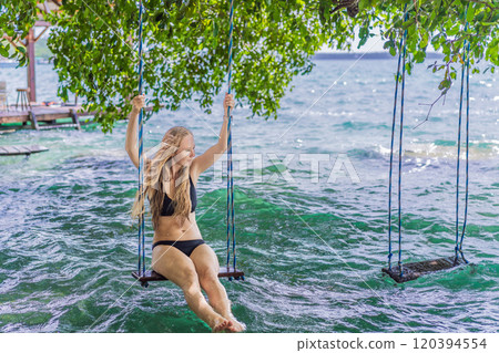 Beautiful female tourist relaxing on a swing in Laguna Bacalar in Mexico during kayak trip. Female tourist swinging over Lake Bacalar with feet in the water. Quintana Roo, Mexico travel, relaxation 120394554