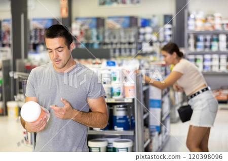 Man buys tin with paint in paintwork material store for carrying out internal finishing work on object 120398096