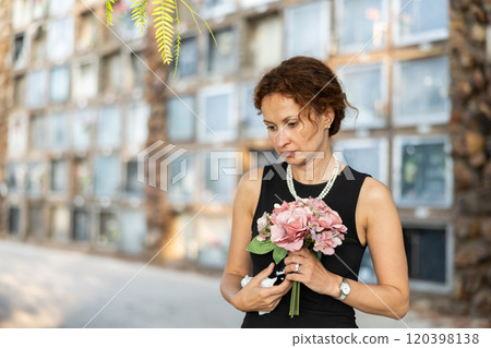 Woman in black mourning dress standing with flowers near columbarium 120398138