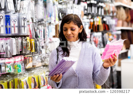 Interested Latina choosing hair rollers in cosmetics boutique 120398217