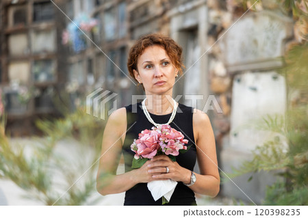 Drieving woman in black dress standing with bouquet by columbarium Drieving woman in black dress standing with bouquet by columbarium 120398235