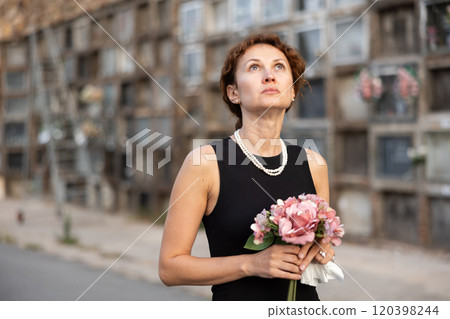 Woman in black mourning dress standing with flowers near columbarium 120398244