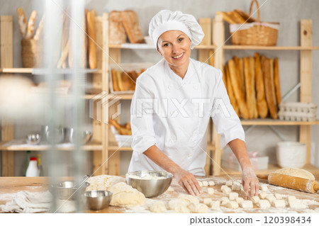 Woman works as baker in bakery, molds pies from dough, creates croissants from dough. 120398434