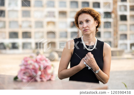 Woman in black dress came to cemetery to lay flowers on grave 120398438