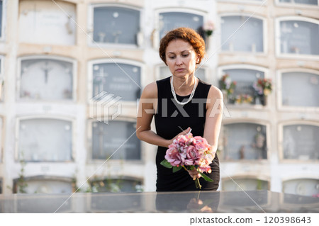Grieving woman in black placing bouquet on grave Grieving woman in black placing bouquet on grave 120398643