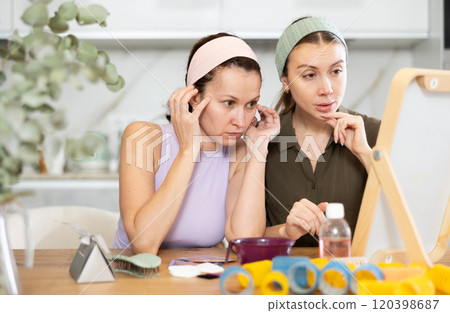 Two adult besties inspecting faces in mirror in cozy home Two adult besties inspecting faces in mirror in cozy home 120398687