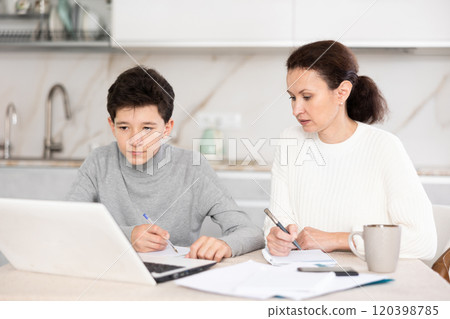Boy and his mother study via video conference using laptop in kitchen 120398785