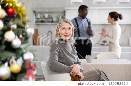 Smiling old woman sitting at the kitchen table with her back to couple quarreling in the kitchen with Xmas-tree 120398814