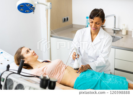 Beautician doing ultrasound lifting procedure in woman's abdominal region 120398888