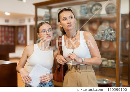 Young woman with teen daughter walk around museum, cookware zone. Young woman with teen daughter walk around museum, cookware zone. 120399100