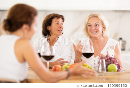 Girlfriends chatting and drinking wine at home party table Girlfriends chatting and drinking wine at home party table 120399160