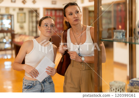 Young woman with teen daughter walk around museum, cookware zone. Young woman with teen daughter walk around museum, cookware zone. 120399161