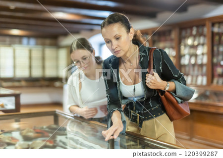 Young woman with teen daughter visitors stands near horizontal glass display case 120399287