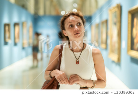 Portrait of beautiful woman looking at pictures and amaze in museum, holding guide book Portrait of beautiful woman looking at pictures and amaze in museum, holding guide book 120399302