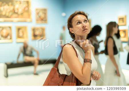 Portrait of beautiful woman looking at pictures and amaze in museum, holding guide book 120399309