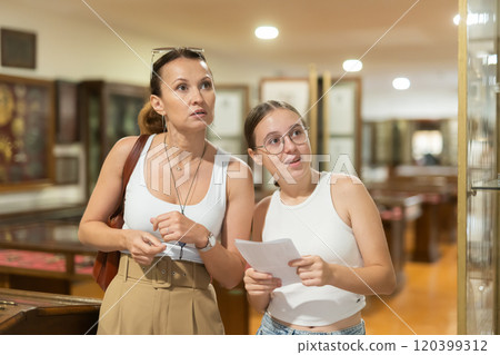 Young woman with teen daughter walk around museum, view antique appliances in museum hall 120399312