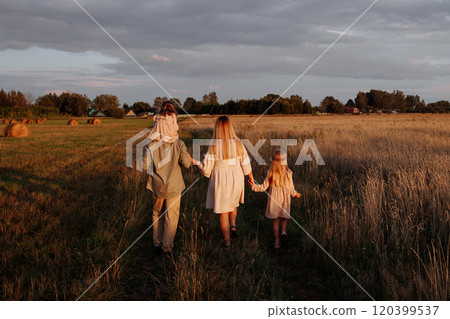 A family of four is walking through a field of tall grass. Rear view. 120399537