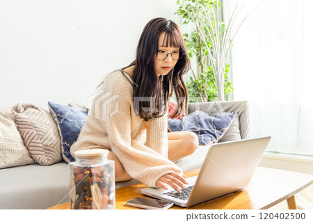 A woman sitting cross-legged on a sofa and using a laptop 120402500