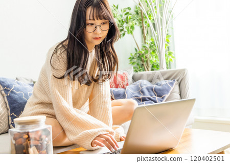 A woman sitting cross-legged on a sofa and using a laptop 120402501
