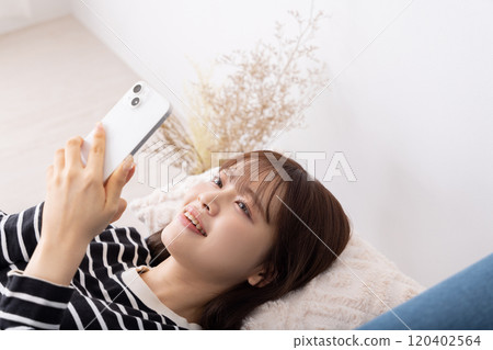 一位女士躺在沙發上使用智慧型手機 一位女士躺在沙發上使用智慧型手機 120402564