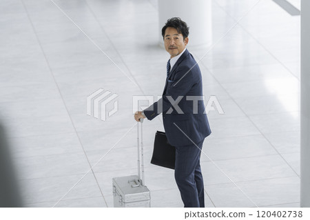 A businessman in his 50s walking with a suitcase and a business bag 120402738