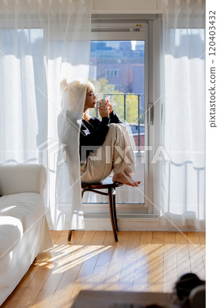 Blonde woman drinking coffee by the window 120403432