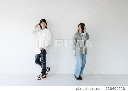 A stylish couple leaning against a white wall 120404210
