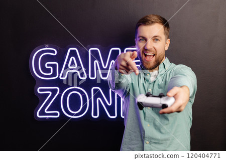 Young bearded man standing at the wall in the room and playing, holding wireless joystick, screaming, and winning intense video game match Young bearded man standing at the wall in the room and playing, holding wireless joystick, screaming, and winning intense video game match 120404771