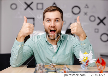 Man with board game piece while practicing strategy in home alone. A man plays a board game with cards and figures, expressing different emotions Man with board game piece while practicing strategy in home alone. A man plays a board game with cards and figures, expressing different emotions 120404774