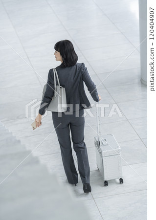 A middle-aged business woman walking with a carry-on bag Back view 120404907