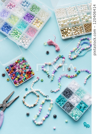 Colorful assortment of beads and jewelry-making tools on a blue surface with completed bracelets 120406414