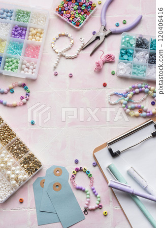 Colorful beads and jewelry making supplies arranged on pink tile background with clipboard and pens Colorful beads and jewelry making supplies arranged on pink tile background with clipboard and pens 120406416