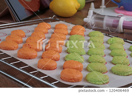 Macarons halves on baking mat on kitchen table. Orange and green cookie cutters for Halloween coloring. Dessert made at home. Macarons halves on baking mat on kitchen table. Orange and green cookie cutters for Halloween coloring. Dessert made at home. 120406469