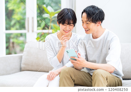 A young couple relaxing in the living room while looking at their smartphones 120408250