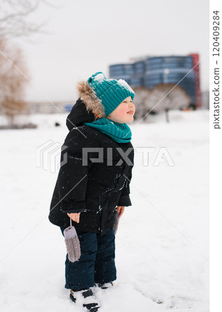 Boy wearing a black coat and a blue hat is standing in the snow. Child is smiling and he is enjoying the winter weather Boy wearing a black coat and a blue hat is standing in the snow. Child is smiling and he is enjoying the winter weather 120409284
