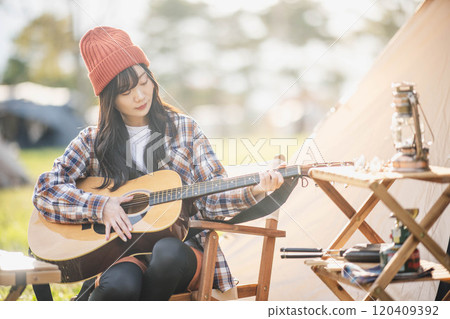 Woman playing guitar at campsite 120409392