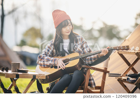 Woman playing guitar at campsite 120409396