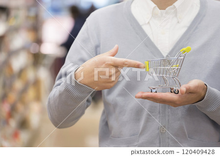 A man's hand pointing at a miniature shopping cart in a supermarket 120409428